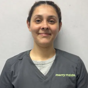 smiling woman with a grey merry maids uniform standing in front of a tan wall